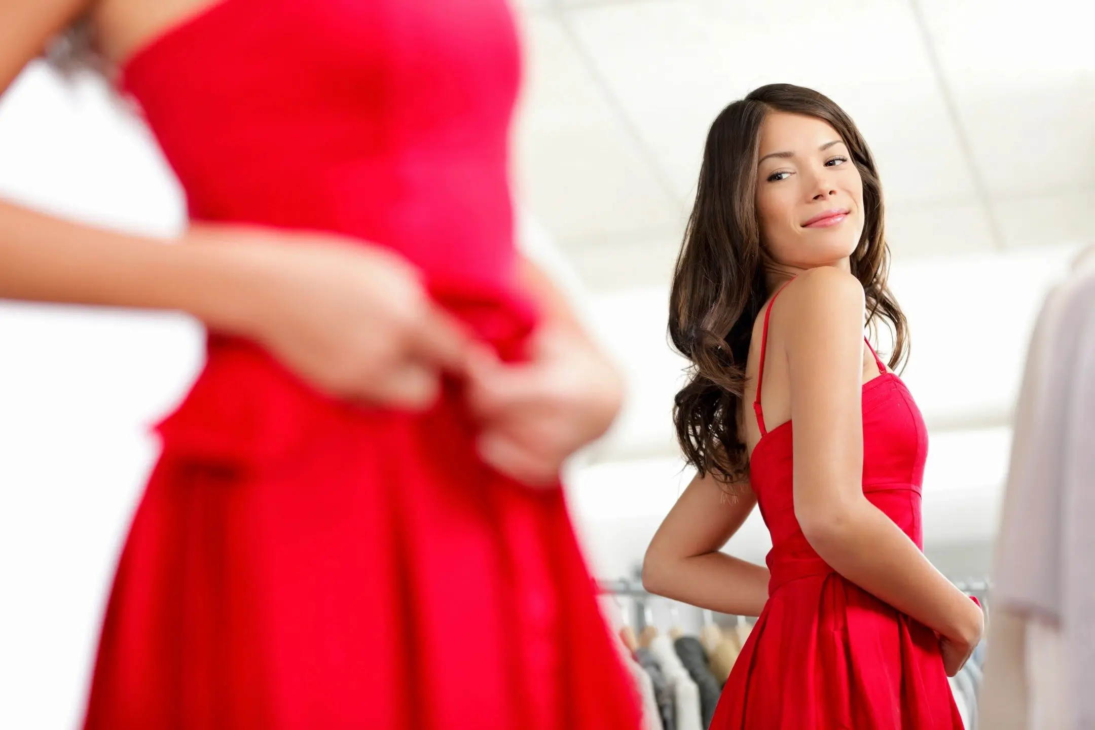 A woman admiring herself in a mirror while wearing a red dress.