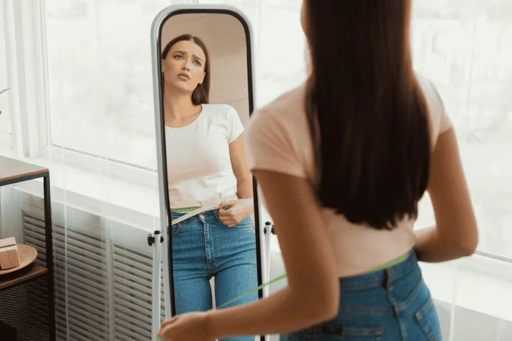 Woman measuring waist with tape in mirror